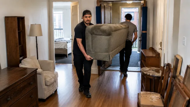 Déménageurs sortant un sofa usagé d’un appartement meublé, devant une commode et des tables