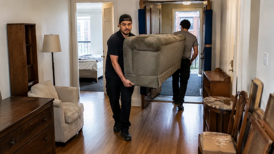 Déménageurs sortant un sofa usagé d’un appartement meublé, devant une commode et des tables